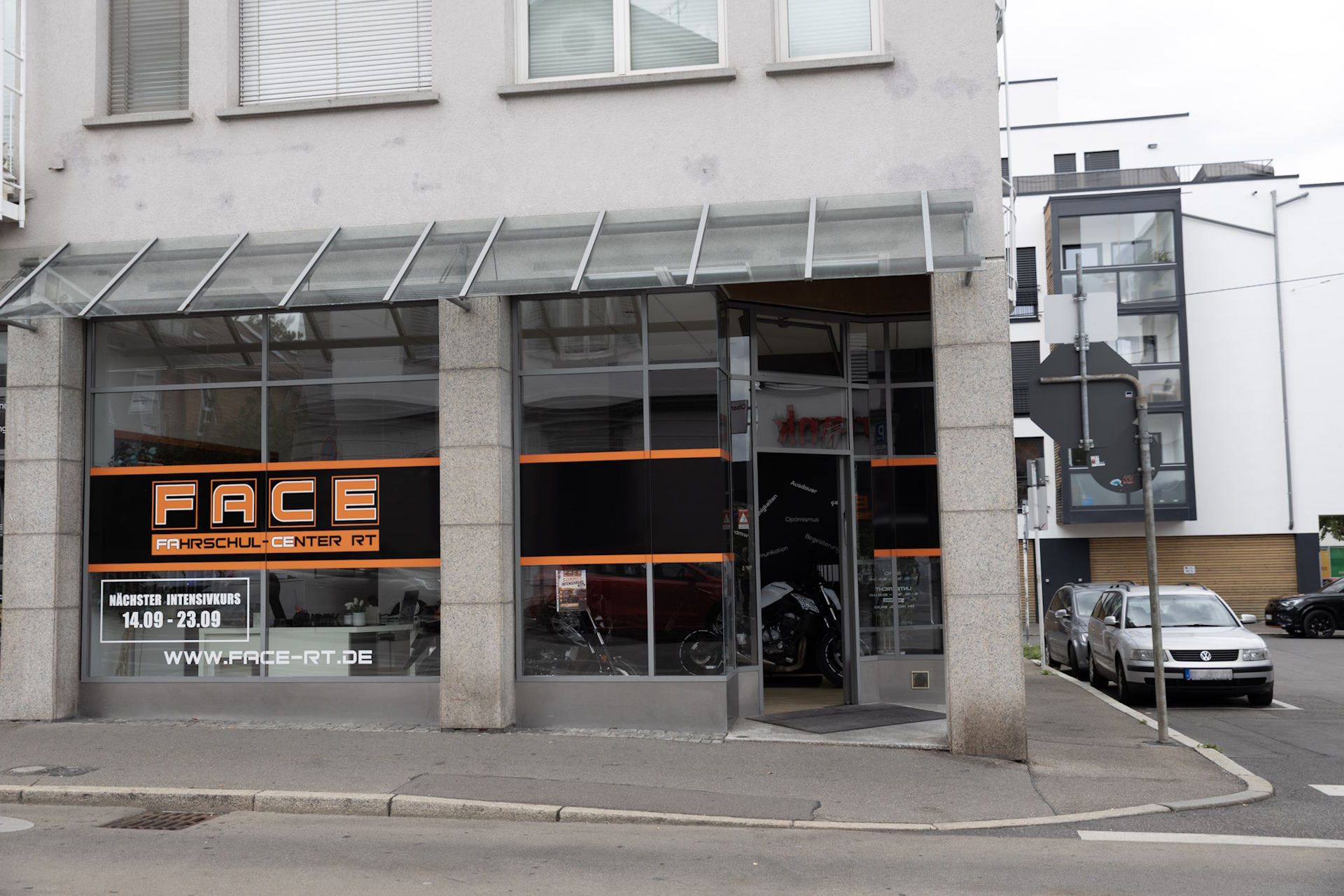 Das Fahrschul-Center FACE von außen: Eckhaus mit großer Fensterfront, orangefarbenem FACE-Schriftzug und dem Eingang unter dem Glasdach